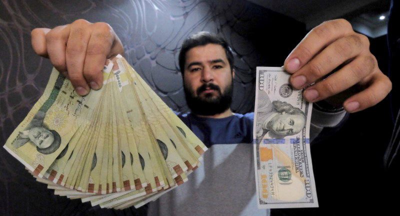 FILE PHOTO: A Money changer poses for the camera with a U.S dollar and the amount being given when converting it into Iranian rials, at a currency exchange shop in Tehran’s business district