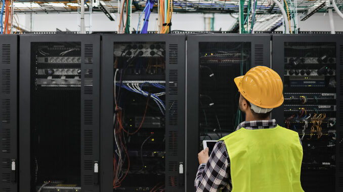 Young technician man working with tablet inside big data center